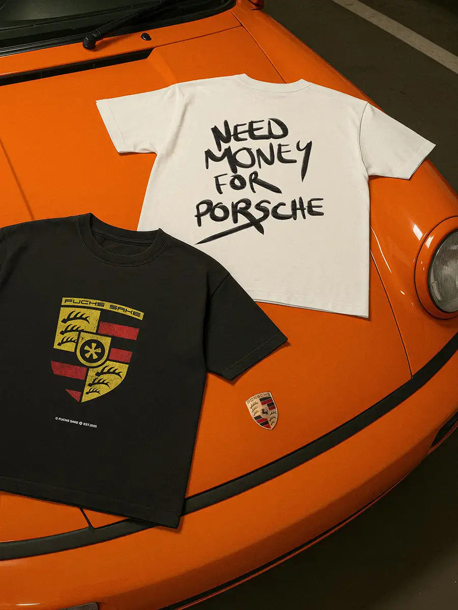Two t-shirts, one black with a logo and one white with text, on an orange Porsche 911, one reads "Need money for porsche" the other shows a Porsche like emblem