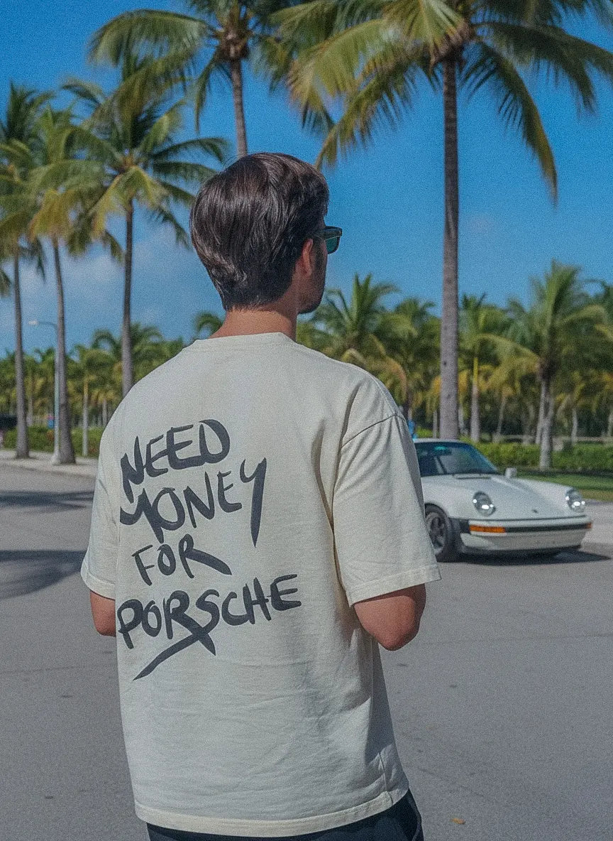 Person wearing a t-shirt with 'NEED MONEY FOR PORSCHE' text, standing in front of palm trees and a vintage car.