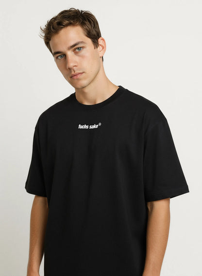 Angled front view of man in casual outfit wearing black ‘fuchs sake’ tee — stylish automotive-inspired clothing celebrating Porsche’s classic Fuchs wheel design.