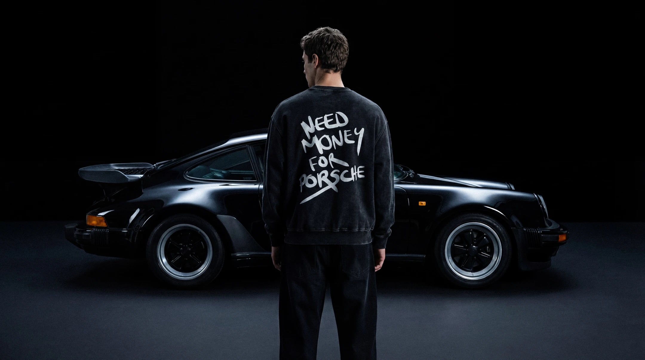 Person wearing a sweatshirt with 'Need Money for Porsche' text standing in front of a classic car.