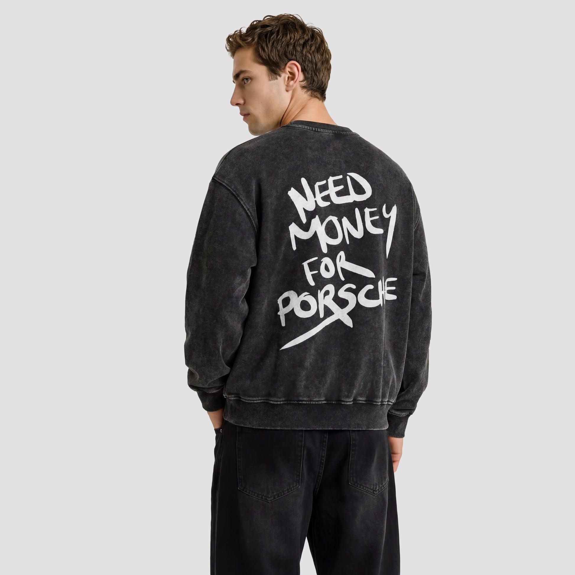 Person wearing a black sweatshirt with 'Need Money for Porsche' text on the back against a beige background