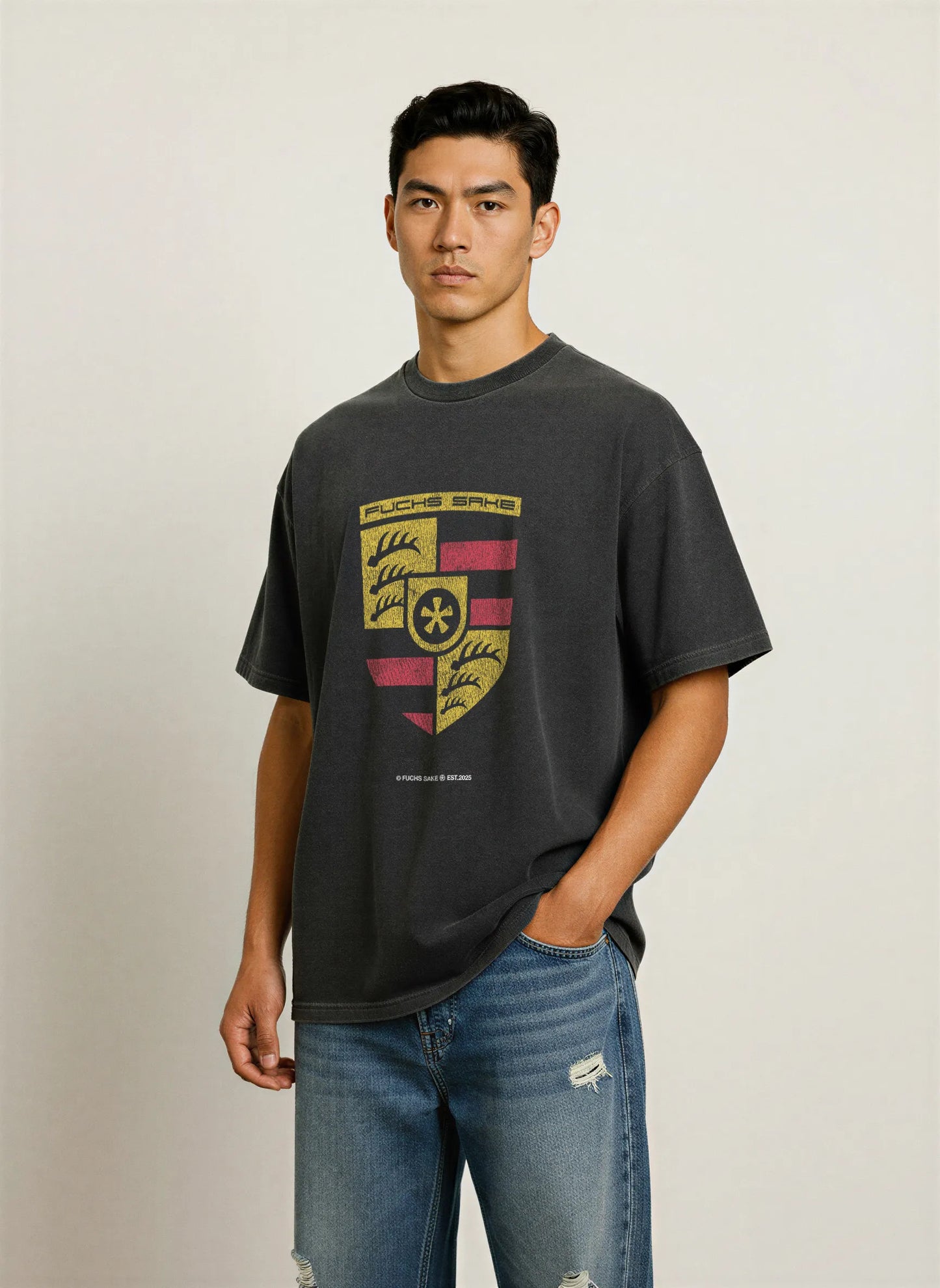 Man wearing charcoal grey T-shirt featuring vintage-style Porsche crest with ‘fuchs sake’ logo — premium automotive streetwear for car enthusiasts.