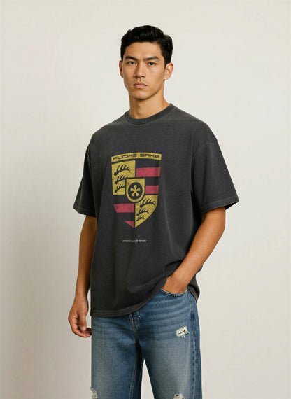 Man wearing charcoal grey T-shirt featuring vintage-style Porsche crest with ‘fuchs sake’ logo — premium automotive streetwear for car enthusiasts.