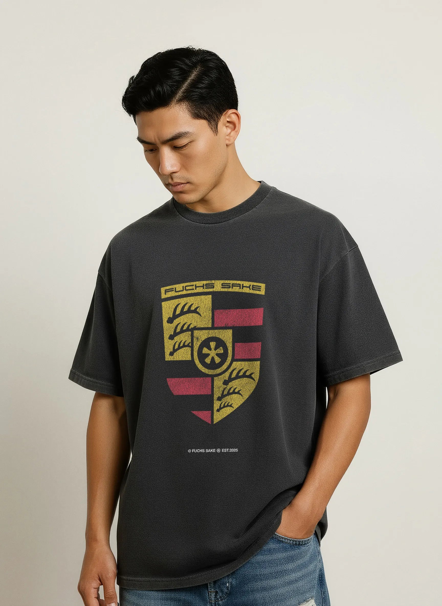 Side view of man modeling dark grey T-shirt with large retro Porsche-inspired crest and ‘fuchs sake’ branding — classic car culture apparel.