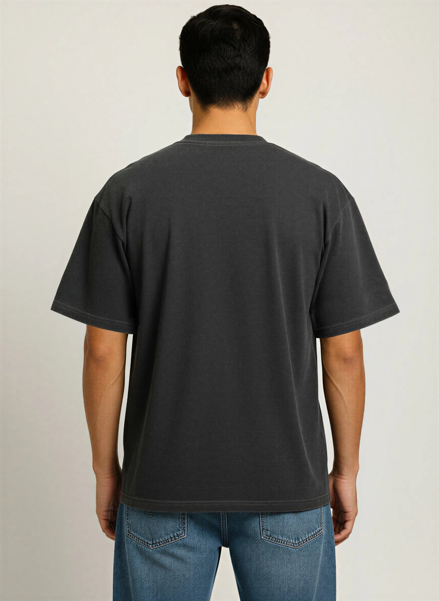 Man wearing a black t-shirt and blue jeans on a plain background