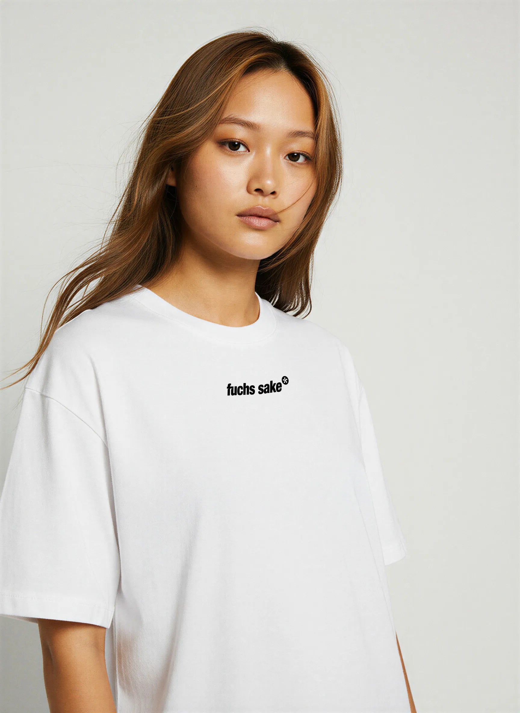 Close-up front view of woman wearing minimalist white T-shirt with small black ‘fuchs sake’ logo on chest — modern car culture clothing inspired by classic Porsche wheels.